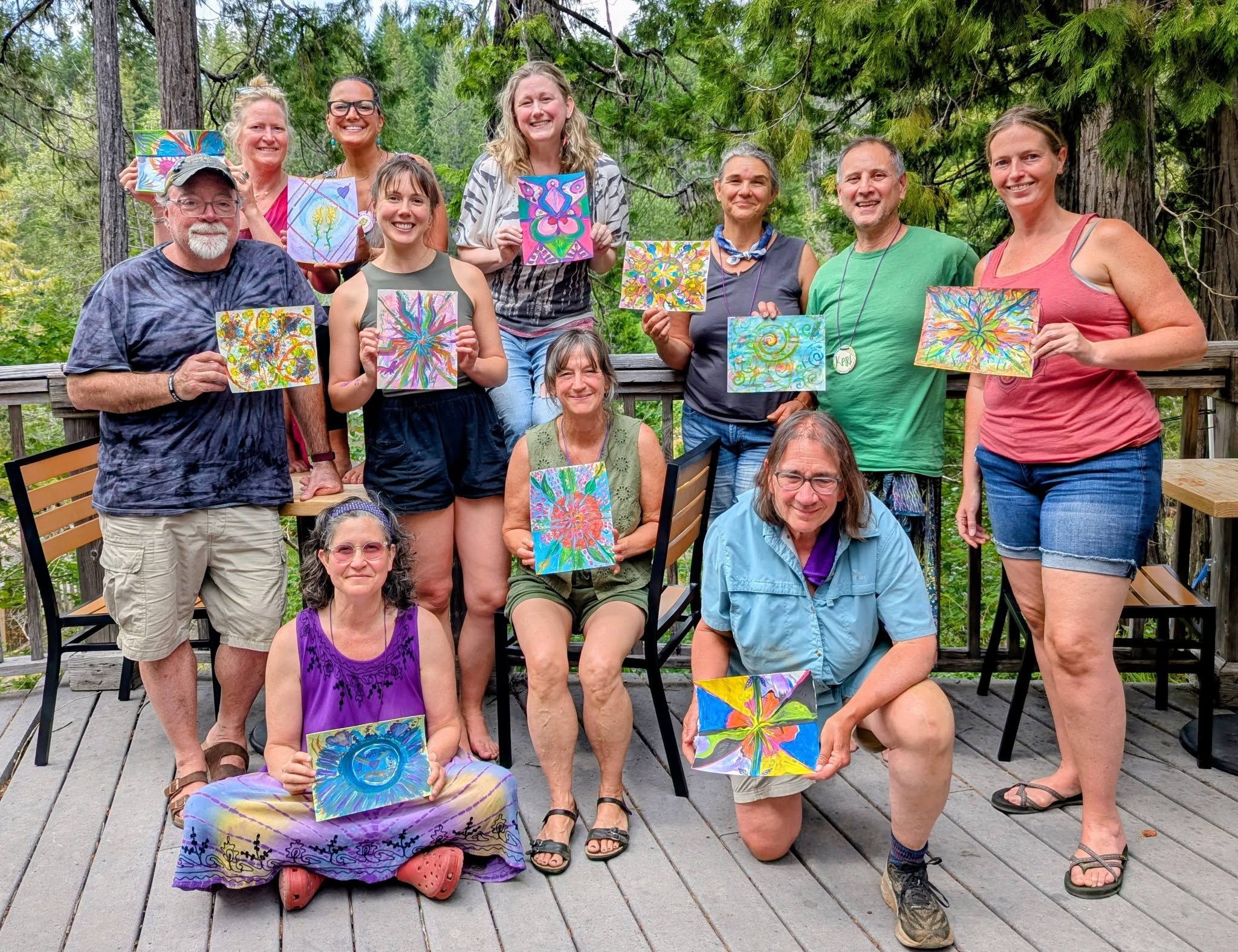 Kindness Portal participants holding their colorful paintings among the trees at Breitenbush Hot Springs